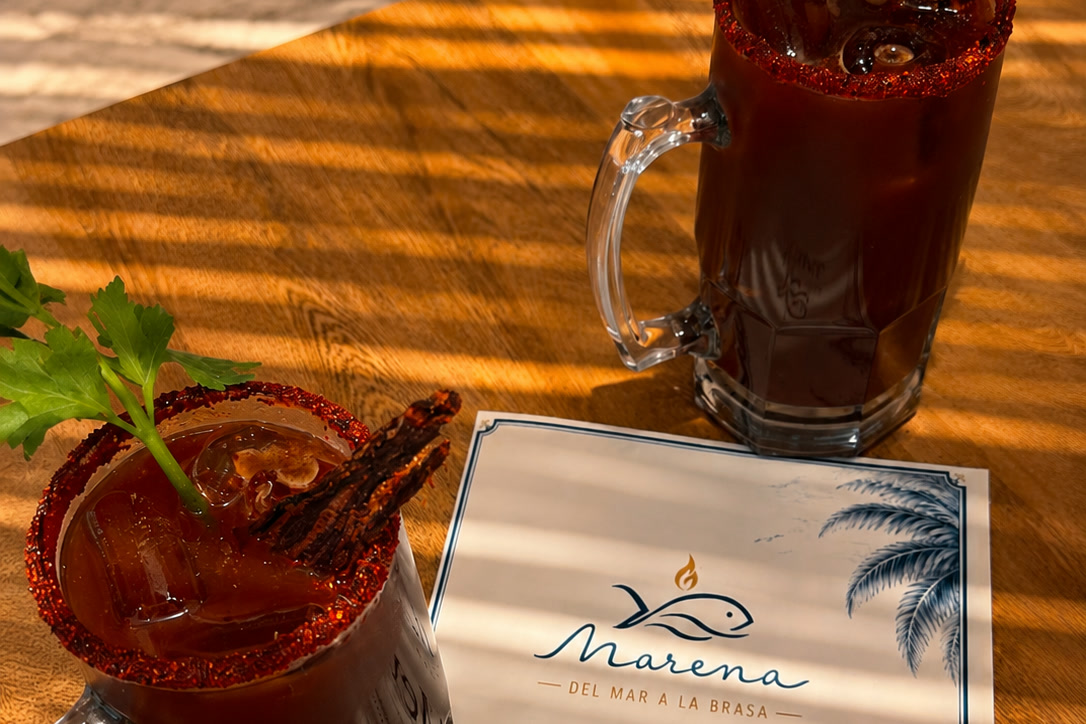 Michelada escarchada junto a la carta impresa de Marena, con la luz de la tarde entrando por la persiana.