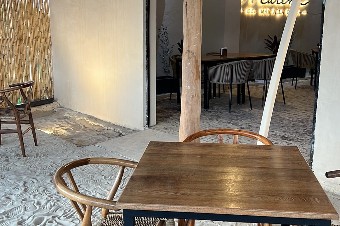 Rincón del salón junto al muro de carrizo, con mesa de madera y sillas de rattan.